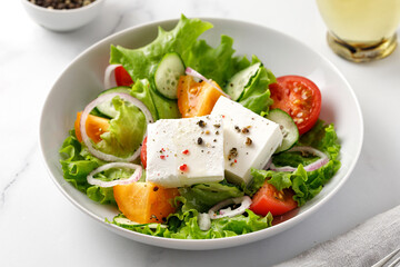 Greek salad in white bowl. Fresh vegetable salad with tomato, onion, cucumbers, pepper, lettuce, feta cheese.