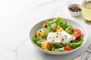 Delicious greek salad with vegetable and feta cheese, close up. Pepper and bottle of oil. Marble background. Copy space