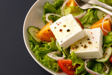 Vegetable salad with cubes feta cheese in white bowl on blue background. Close up