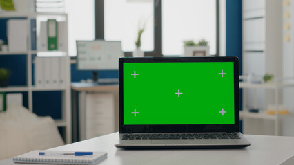 Close up of green screen on laptop at empty desk. Nobody at desk with chroma key and isolated mock up template, blank background on laptop. Business space with chromakey display.