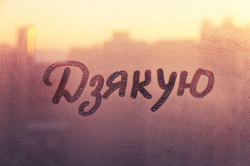 Ukrainian language word thanks in english are painted on wet orange sunrise glass of window