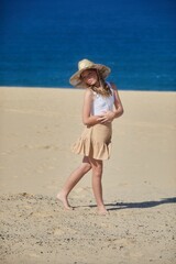 Fototapeta premium A young girl wearing a hat and skirt has fun being sassy on a sandy beach
