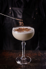 Bartender dressed in black apron and shirt make white cocktail drink on black background