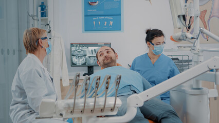 Obraz premium Stomatologist and nurse finishing oral care procedure with patient in dentistry office. Dentist giving mirror to man to look at denture results after surgery and dental examination.