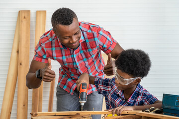 African black male carpenter man father teach boy kid child son to be carpenter drilling wood in carpentry workshop. Concept hobby at home.