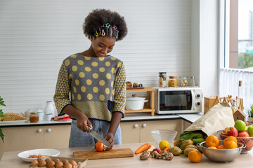 Young beautiful African black girl woman cutting tomato in kitchen for cooking, food and meal preparation.