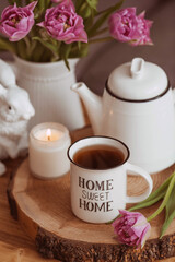 Fototapeta na wymiar Still-life. A vase with flowers, tulips, a teapot, a bunny, a candle and a cup of tea on the coffee table in the living room home interior. Cozy spring concept.