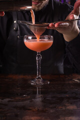 Bartender dressed in black apron and shirt make cocktail drink on black background