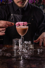 Bartender dressed in black apron and shirt is decorating cocktail drink on black background