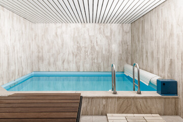 Indoor modern small swimming pool in light grey sauna interior.