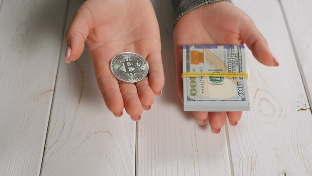 Close-up of a silver bitcoin and a stack of hundred dollar bills in the hands of a young woman. Bitcoin and cryptocurrency trading concept.