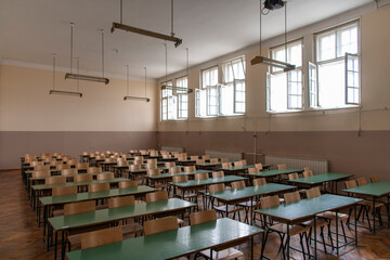Empty old faculty or college School classroom with row of chairs, green desk tables and big white windows. Natural light.
