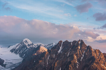 Vivid alpine landscape with high snow rocky pinnacle in gold sunrise colors. Colorful mountain scenery with sunlit golden rocks and snowy mountain peak at sunrise. Early morning at very high altitude.