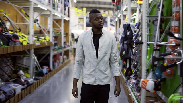 African American man walking along shelves in hardware store and examines goods