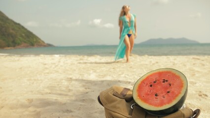 Naklejka na ściany i meble The cheerful woman in blur, against the background of a watermelon on tropical sand beach sea. Portrait attractive beautiful girl caucasian spend summer weekend in outdoor. White shirt beachwear.