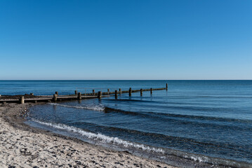 baltic sea sandy beach with bathing jetty and wooden breakwater against clear blue sky