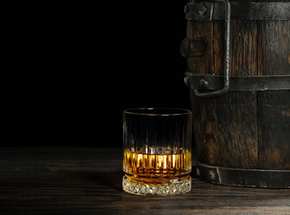 Aged scotch whiskey and old wooden keg on dark background