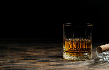 Glass of aged alcoholic scotch whiskey on wooden table and black background