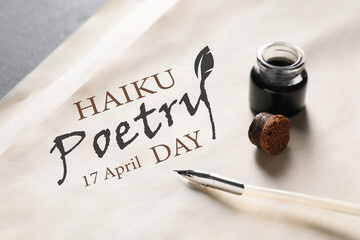 Paper sheet with text HAIKU POETRY DAY 17 APRIL and feather pen with inkwell on table, closeup - obrazy, fototapety, plakaty