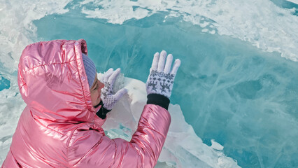 Girl walking on cracked ice of frozen lake Baikal. Woman traveler explores and looks at an ice floe. Magic purest place in nature. Ice arounds traveler all his trip. Hiker walk in cosmic pink jacket.