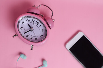 Mobile phone, earphone and alarm clock on pink background