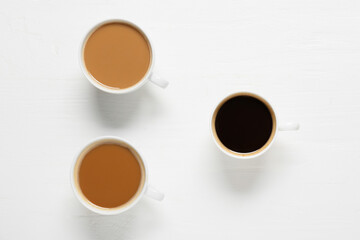 Different cups of coffee on white wooden background. Concept of racism