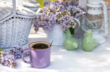The postcard is beautiful. A fancy purple coffee mug, an old book and a bouquet of purple lilac. Beautiful still life. Spring time. The concept of 