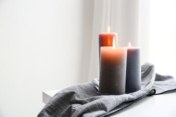 Burning candles with napkin on table in light room