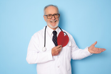 Senior age handsome grey-haired doctor man holding heart of red paper with a happy face standing and smiling with a confident smile showing teeth. Medical concept.