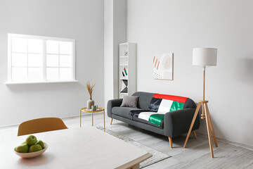 Interior of light living room with black sofa, dining table and UAE flags