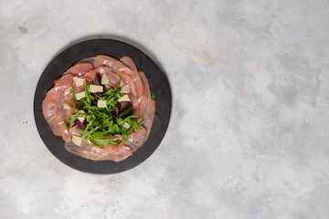Slices of beef tenderloin, with arugula leaves, parmesan and spices. On a gray background, top...