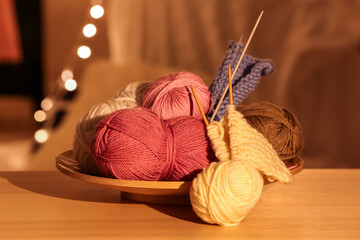 Plate with knitting yarn and needles on wooden table