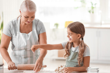 Mature woman with her little granddaughter rolling out dough in kitchen