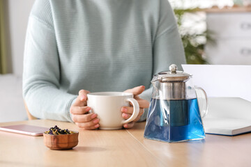 Woman drinking tasty blue tea at table
