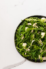 Delicious light salad with arugula, mozzarella and chicken breast in a plate on a white marble background, top view