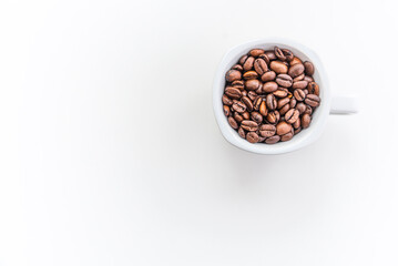 A white coffee cup filled with coffee beans on a white minimalist background