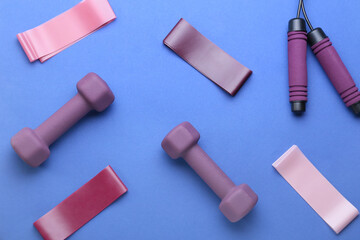 Stylish dumbbells, skipping rope and elastic bands on blue background