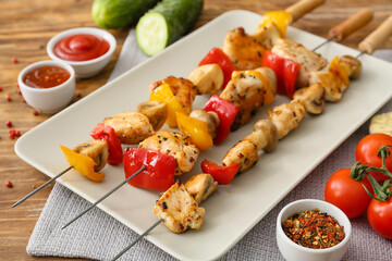 Plate of grilled chicken skewers with vegetables on wooden background