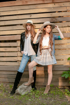 Two teenage girls wearing country style clothes standing against wooden planks wall background