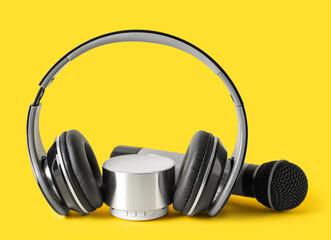 Wireless portable speaker, headphones and microphone on yellow background