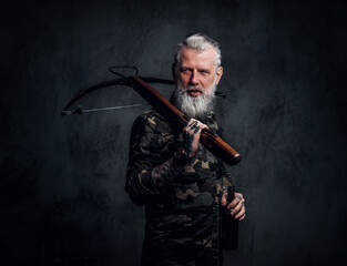 Bearded old man with grey hairs holding crossbow on his shoulder