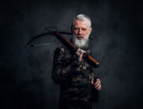 Bearded old man with grey hairs holding crossbow on his shoulder