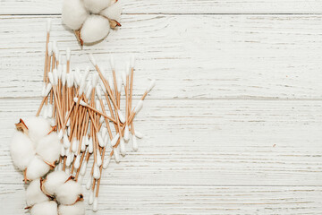 Cosmetic eco sticks on a cardboard base are scattered with cotton on a white background.