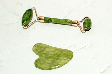massage stone jade gouache scraper and facial roller light background.