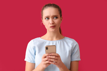 Thoughtful young woman with mobile phone on red background