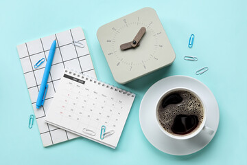 New alarm clock with cup of coffee and stationery on blue background