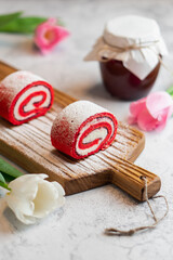 Homemade pink cupcakes on wooden board with spring tulips and jar of jam on gray background