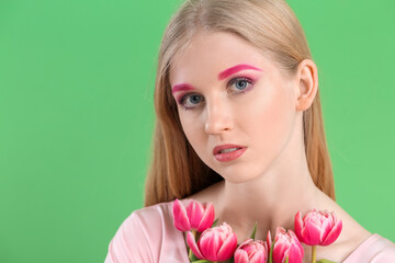 Young woman with creative makeup and beautiful tulips on green background