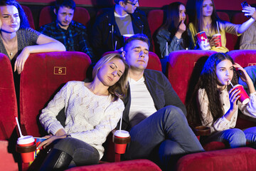 Young people watching a boring movie at the cinema, guy and girl is sleeping