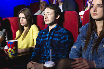 Friends a man and a woman are watching a movie in a movie theater crying.